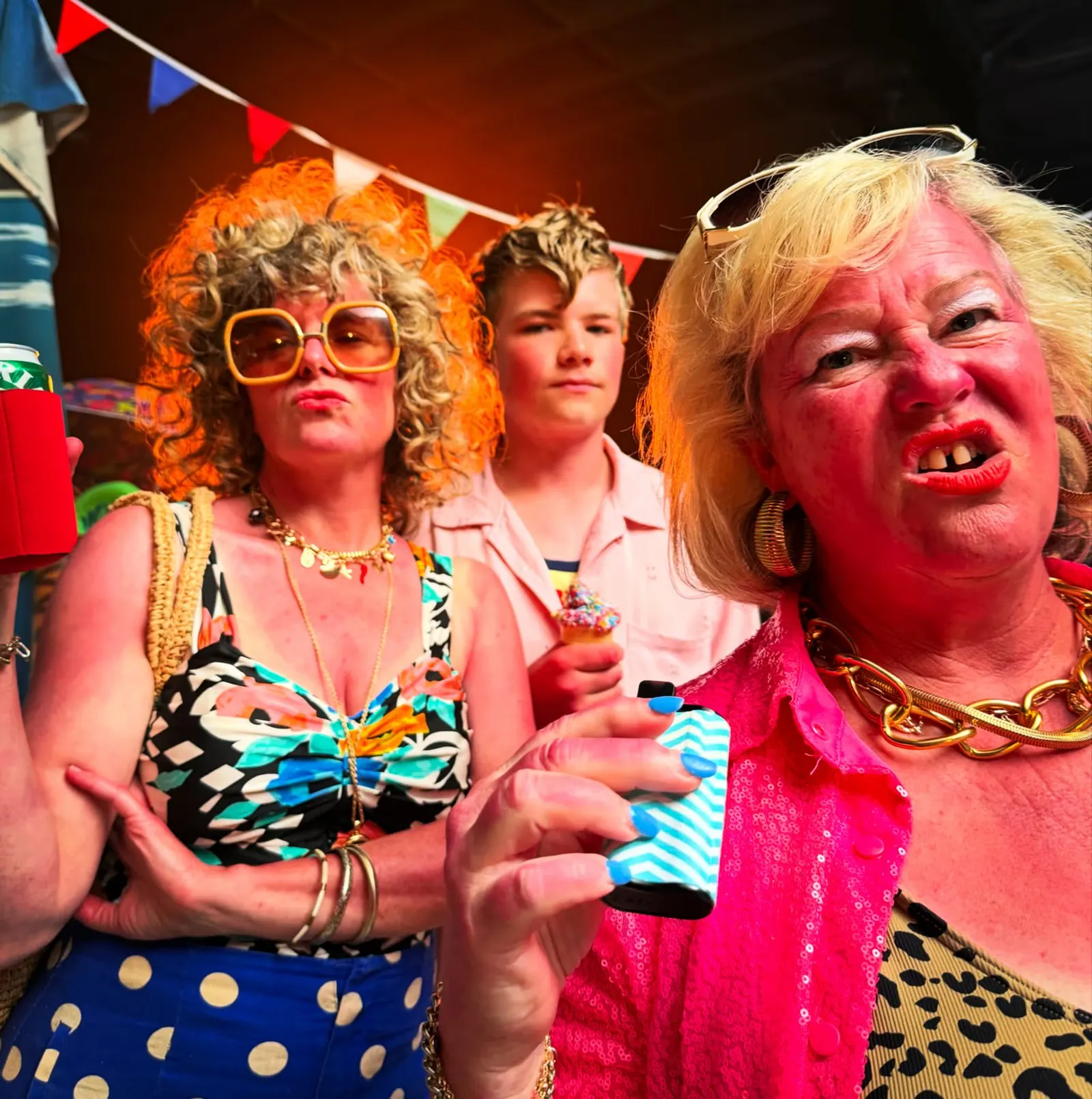 Holiday: three holidaymakers in loud prints and sunglasses pull faces under party bunting