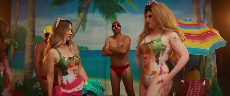 Holiday: a woman and a drag performer in matching body-print swimsuits pose beside men in red trunks