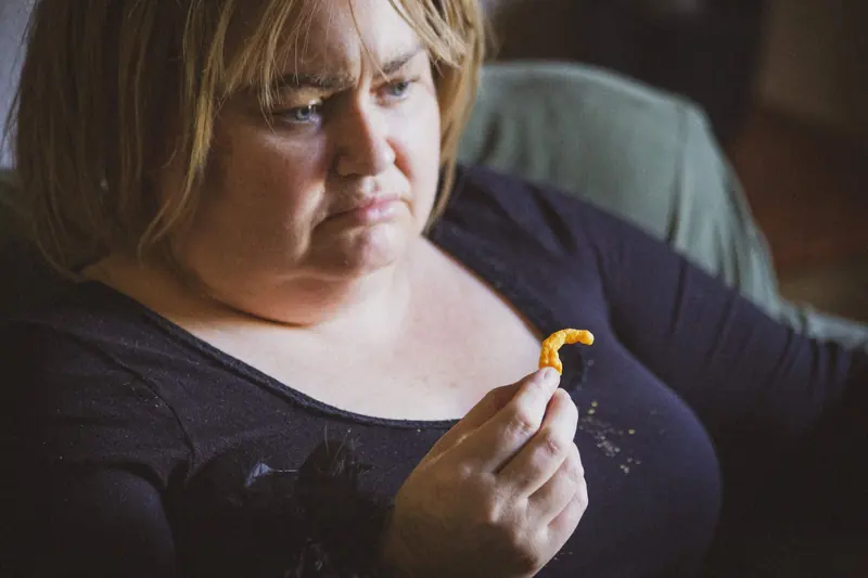 Maggie May: a woman in a dark top looks down at a cheese snack in her hand