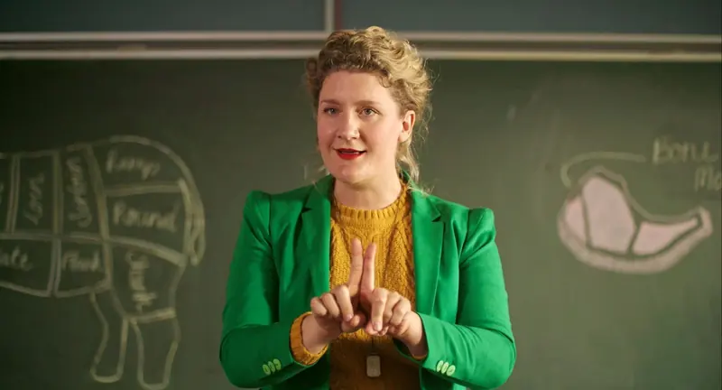 Mrs McCutcheon: a teacher in a green blazer speaks in front of a chalkboard