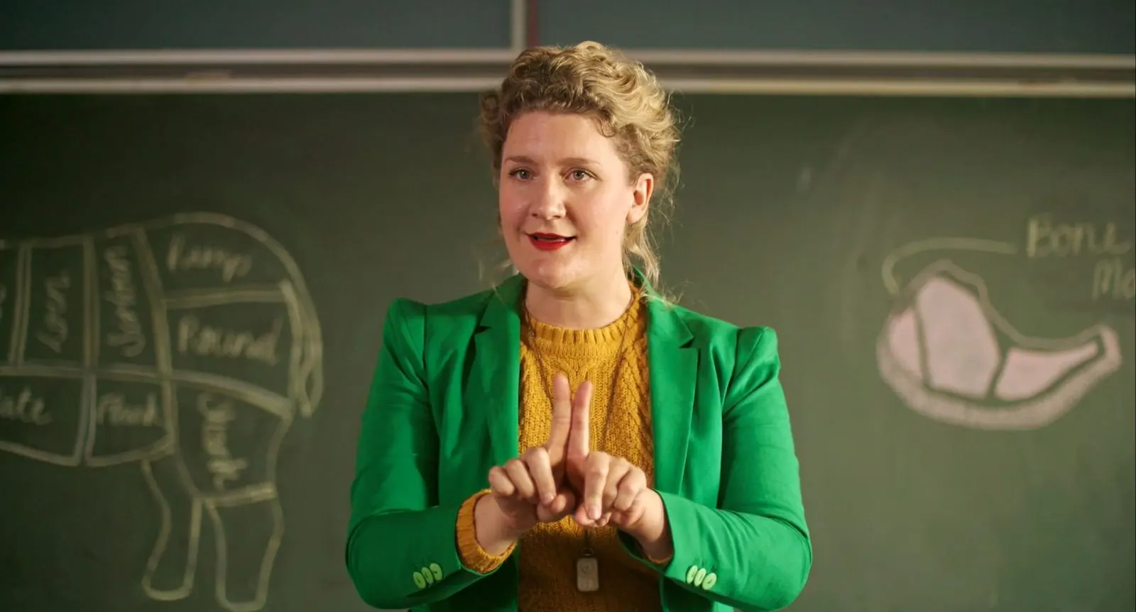 Mrs McCutcheon: a teacher in a green blazer speaks in front of a chalkboard