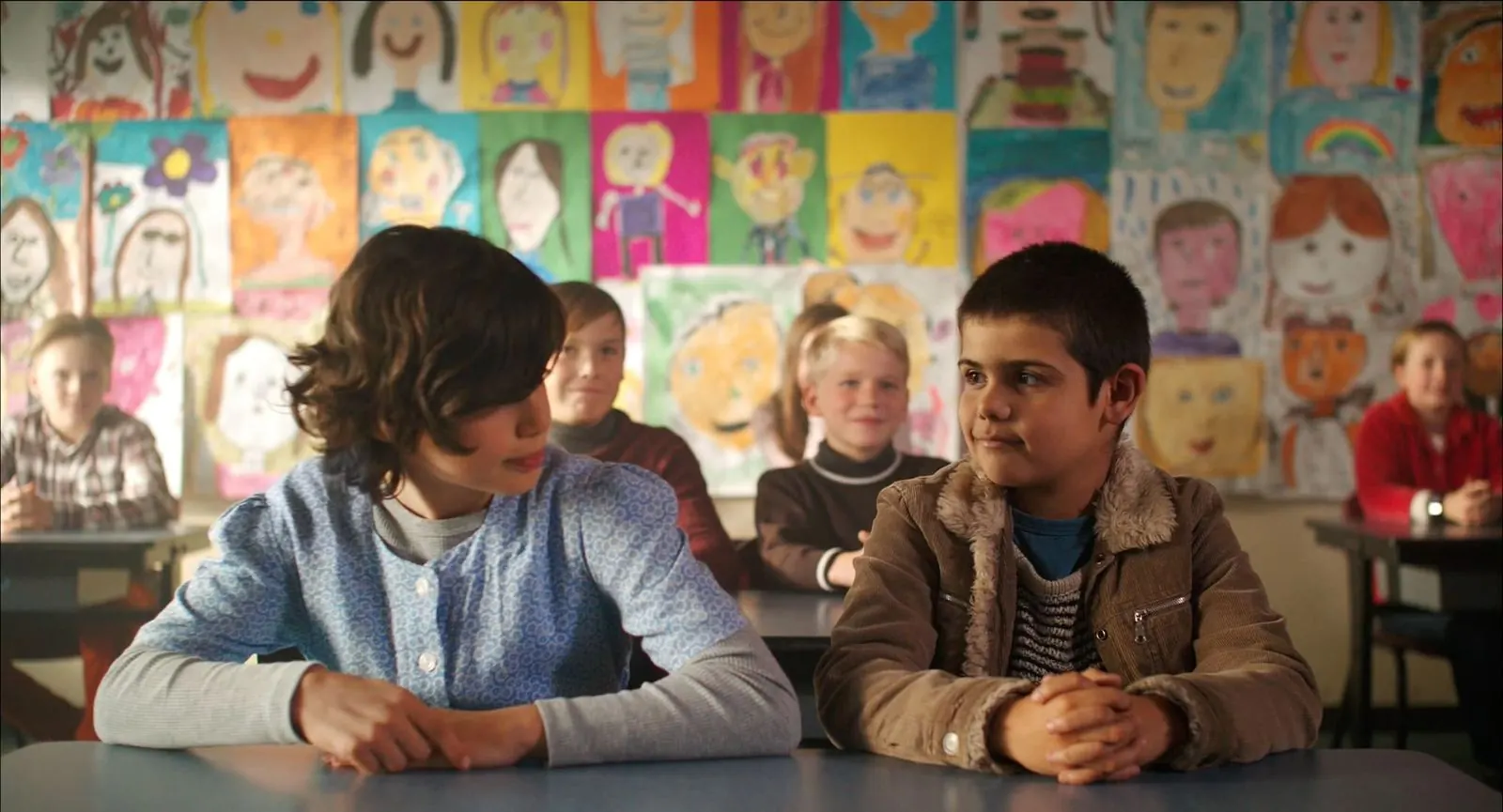 Mrs McCutcheon: two children sit at a classroom desk in front of a wall of drawings