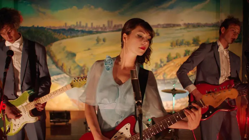 Mrs McCutcheon: a woman sings and plays guitar with a band on a school stage