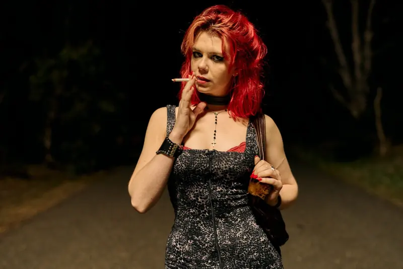 Penny Lane Is Dead: a red-haired young woman in a sequinned dress smokes on a dark road at night