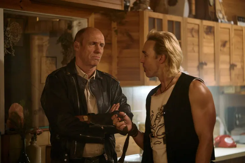 Penny Lane Is Dead: two men face off in a wood-panelled kitchen, one in a leather jacket with arms folded