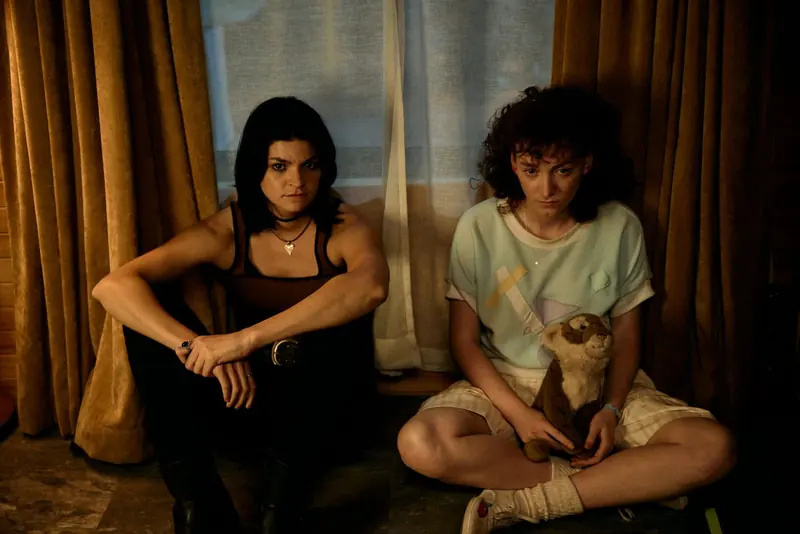 Penny Lane Is Dead: two young women sit on the floor against curtains, one holding a toy otter