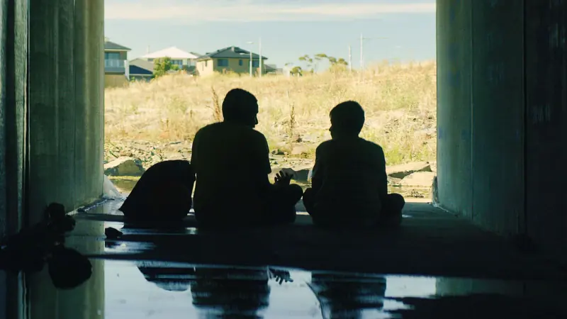 Tarneit: two boys sit silhouetted in a concrete underpass looking out at new houses